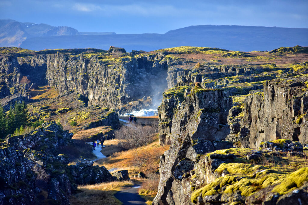 Wanderer laufen auf einem Weg zwischen hohen Felswänden und moosigen Klippen.