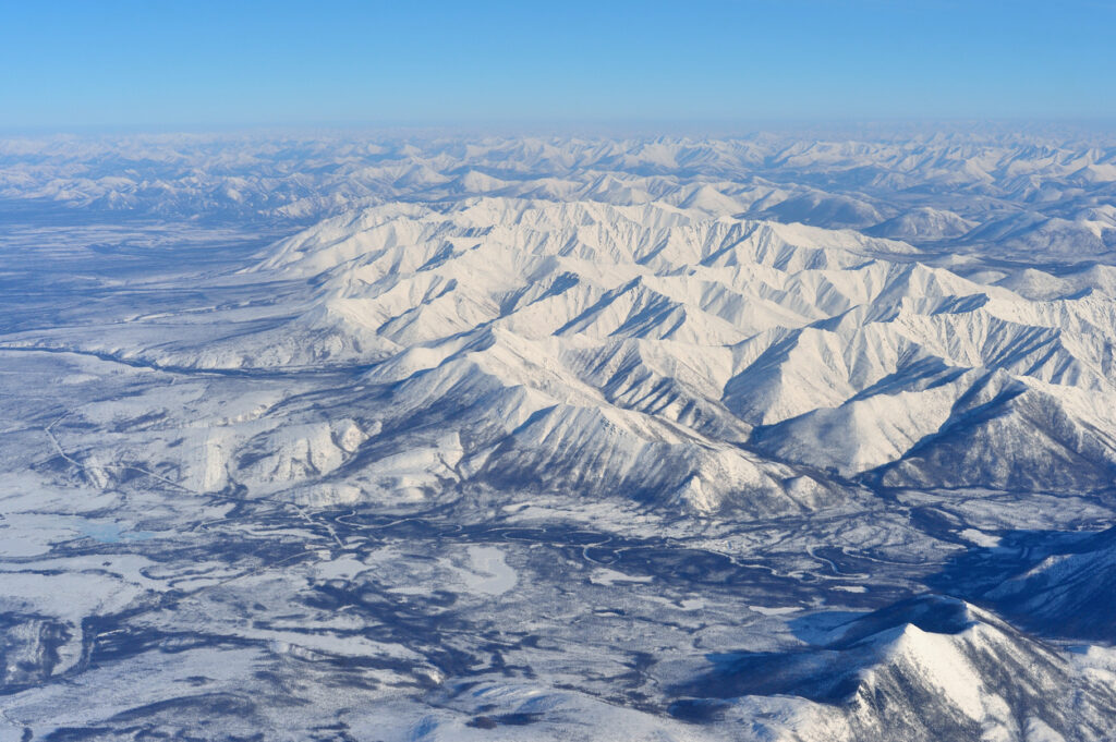 Eine endlose, schneebedeckte Berglandschaft erstreckt sich nahe Oimjakon unter blauem Himmel.