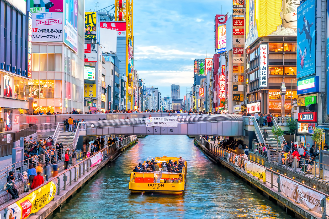 Ein Boot fährt auf dem Dotonbori-Kanal unter einer Brücke durch Osakas Neonviertel.