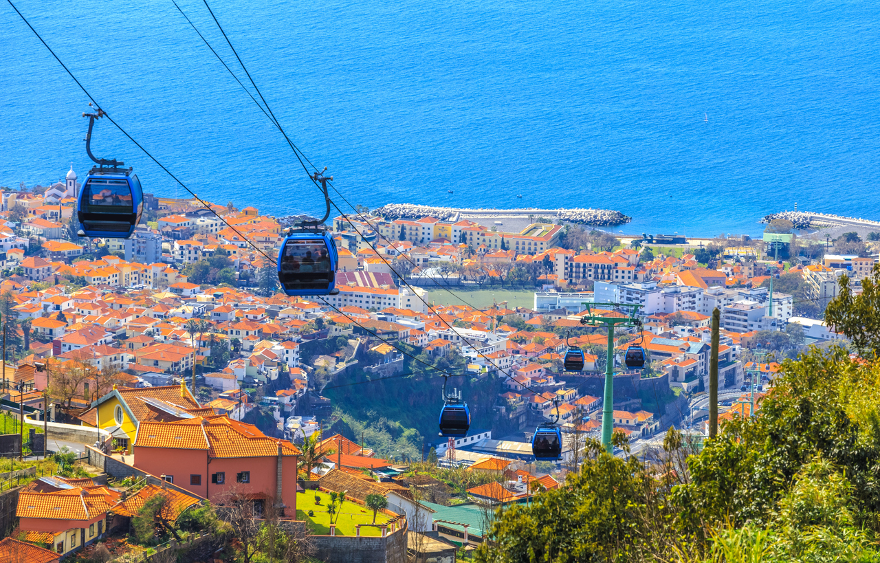Gondeln der Seilbahn schweben über den Dächern von Funchal Richtung Atlantik.