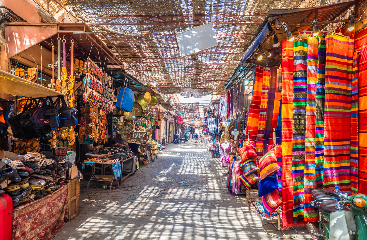 Bunte Stoffe und Handwerk hängen in einer schattigen Souk-Gasse in Marrakesch.