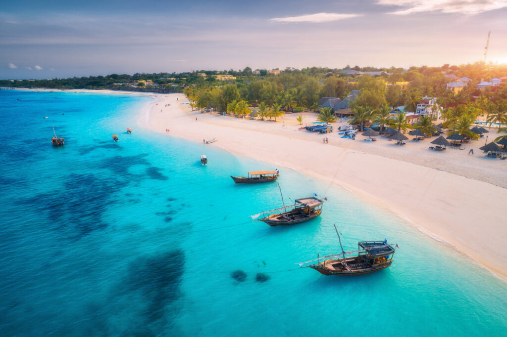 Traditionelle Boote liegen im klaren Wasser, während ein breiter Strand bei Sonnenlicht auf Sansibar leuchtet.