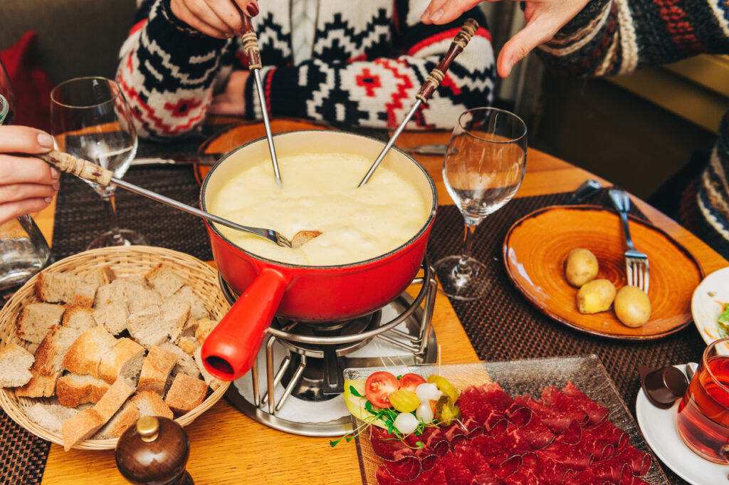 Mehrere Hände tauchen Brotstücke mit Fonduegabeln in einen roten Topf mit cremigem Schweizer Käsefondue.