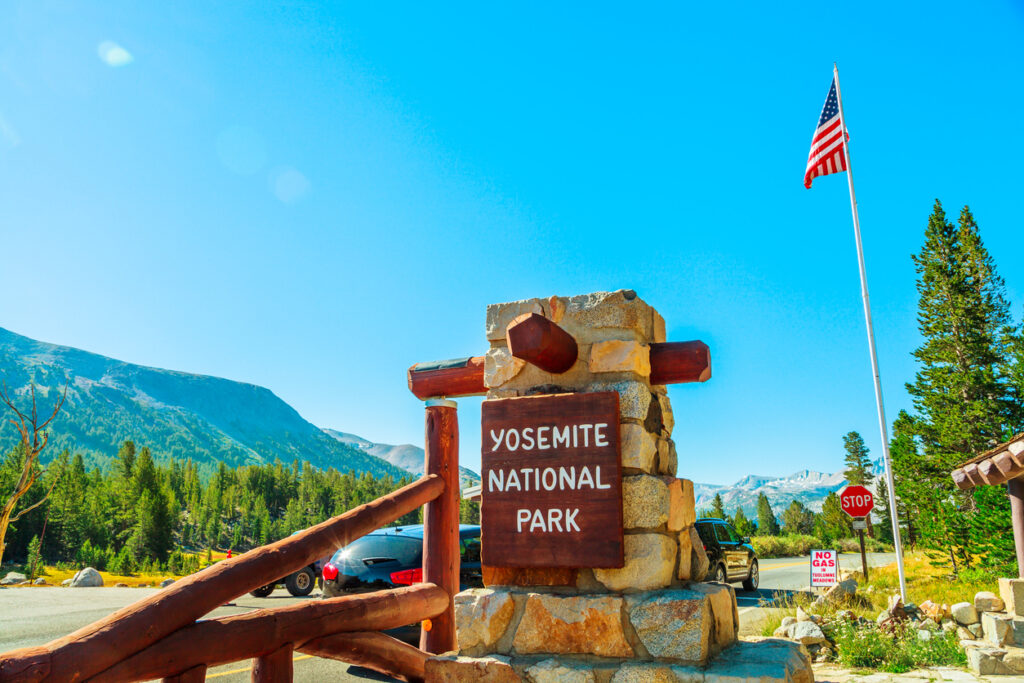 Ein steinernes Schild mit der Aufschrift „Yosemite National Park“ steht an der Einfahrt unter blauem Himmel.