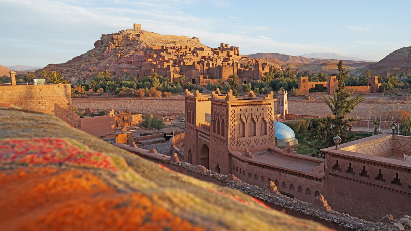 Die Lehmfestung Aït-Ben-Haddou nahe Marrakesch liegt warm beleuchtet vor den Bergen.