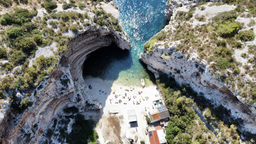 Drohnenblick auf eine kleine Kiesbucht in Kroatien mit türkisblauem Wasser und steilen Felsen.