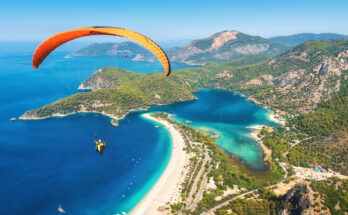 Ein orangefarbener Gleitschirm schwebt über Strand und Lagune an der Küste.