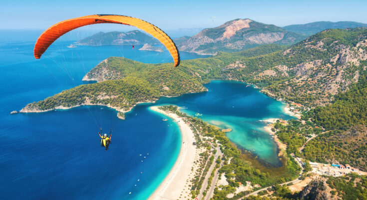 Ein orangefarbener Gleitschirm schwebt über Strand und Lagune an der Küste.