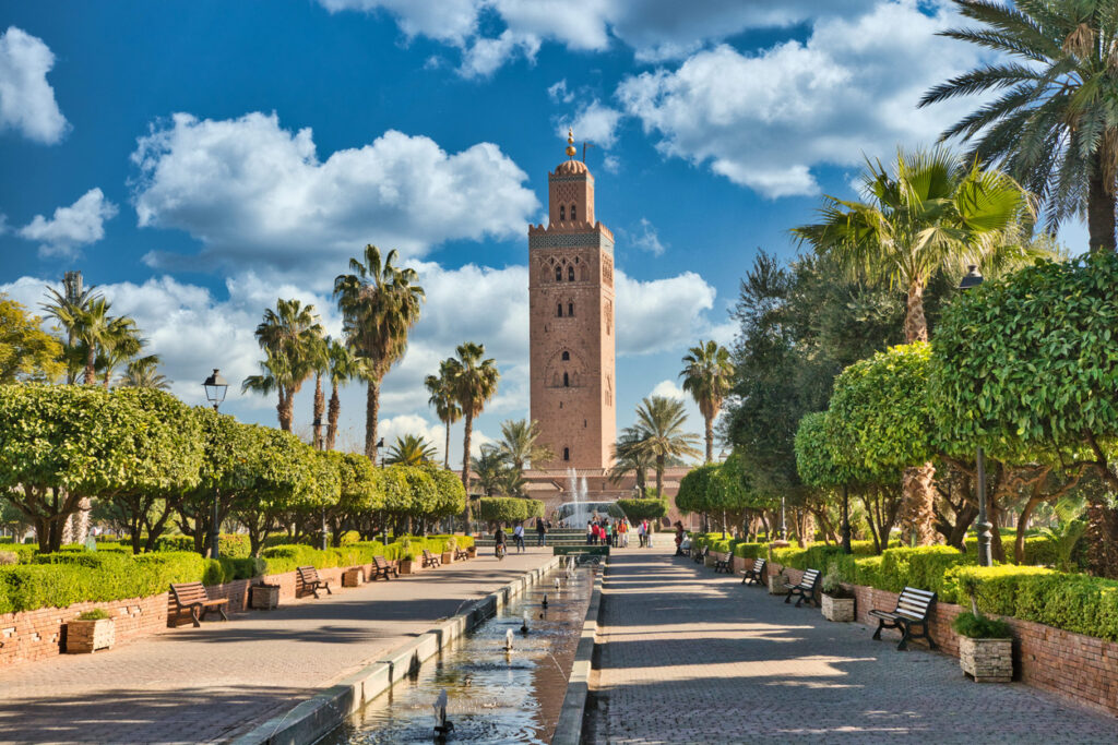 Das Koutoubia-Minarett ragt über eine Palmenallee und Brunnen in Marrakesch.