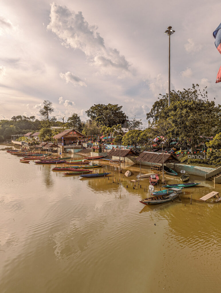 Am Khlong Hae Floating Market liegen viele bunte Boote am ruhigen Flussufer im warmen Abendlicht.