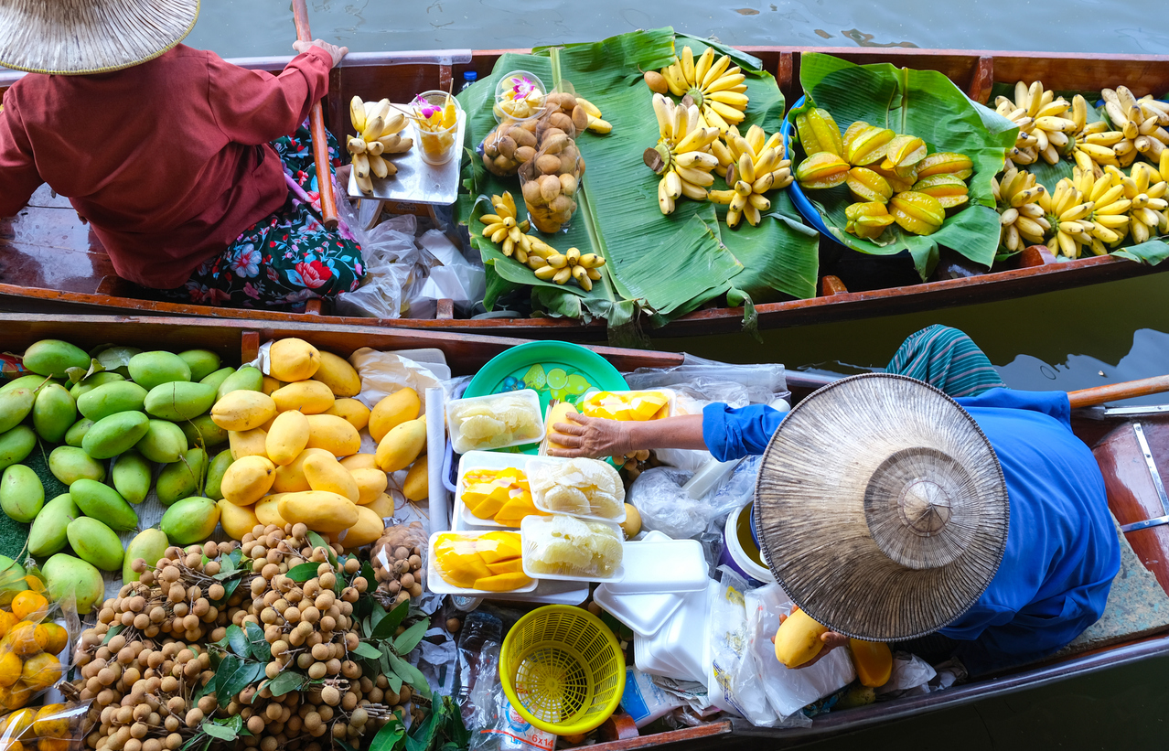 Zwei Verkäufer in Booten mit Bananen, Mangos und Longan auf dem Damnoen Saduak Floating Market.