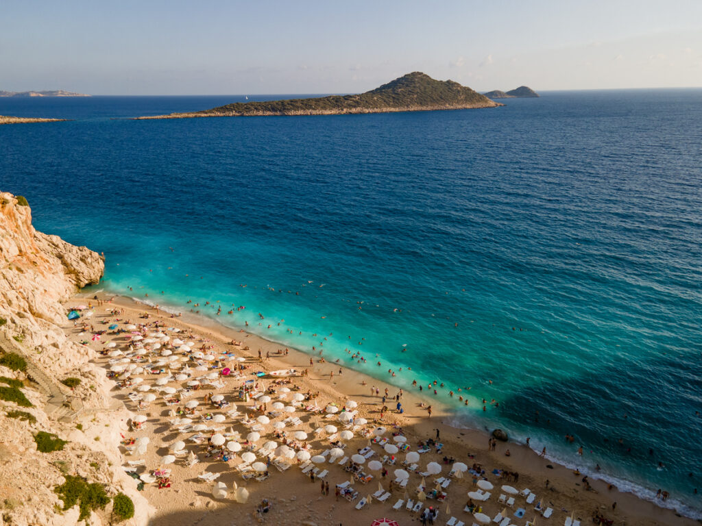 Viele Sonnenschirme stehen am Kaputaş Beach, dahinter glitzert das tiefblaue Meer.