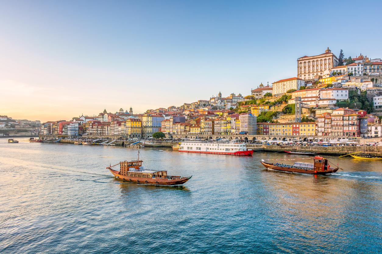Boote fahren auf dem Douro vor der farbenfrohen Uferpromenade von Porto im warmen Abendlicht.