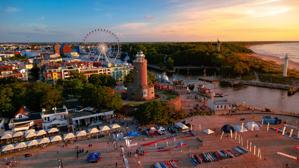 Der Leuchtturm und ein Riesenrad leuchten am Abend über dem Hafen von Kolberg.