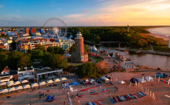 Der Leuchtturm und ein Riesenrad leuchten am Abend über dem Hafen von Kolberg.
