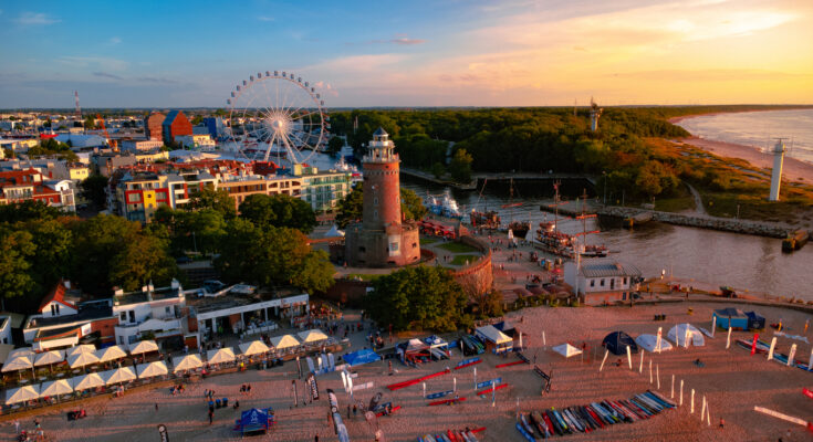 Der Leuchtturm und ein Riesenrad leuchten am Abend über dem Hafen von Kolberg.