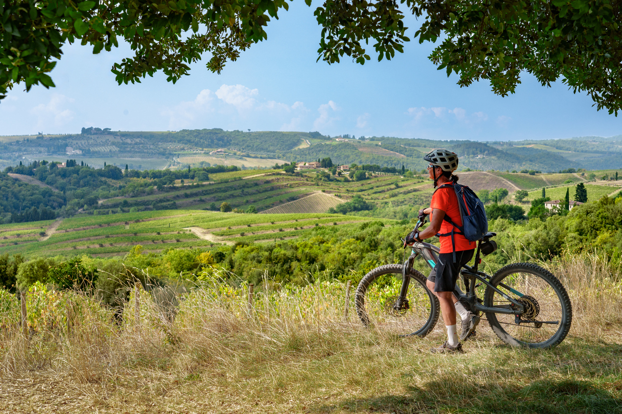 Eine Radfahrerin steht am Weg und schaut über Weinberge in der Toskana.