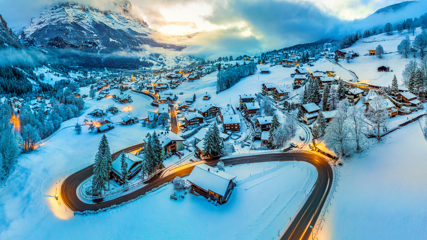 Winterlicher Blick auf Grindelwald mit verschneiten Chalets, kurviger Straße und Bergen im Abendlicht.