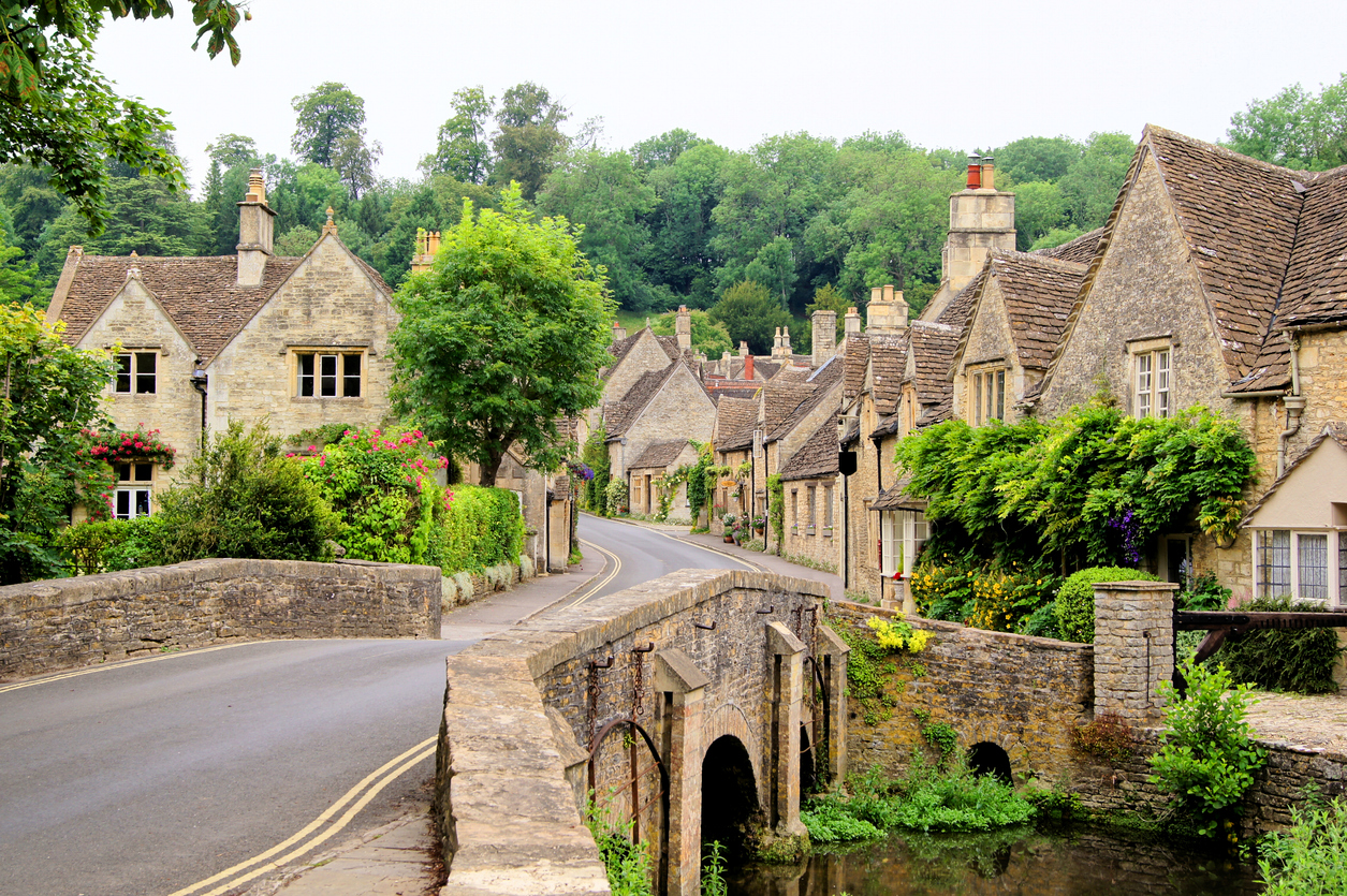 Steinbrücke und honigfarbene Cottages säumen eine ruhige Straße in den Cotswolds.