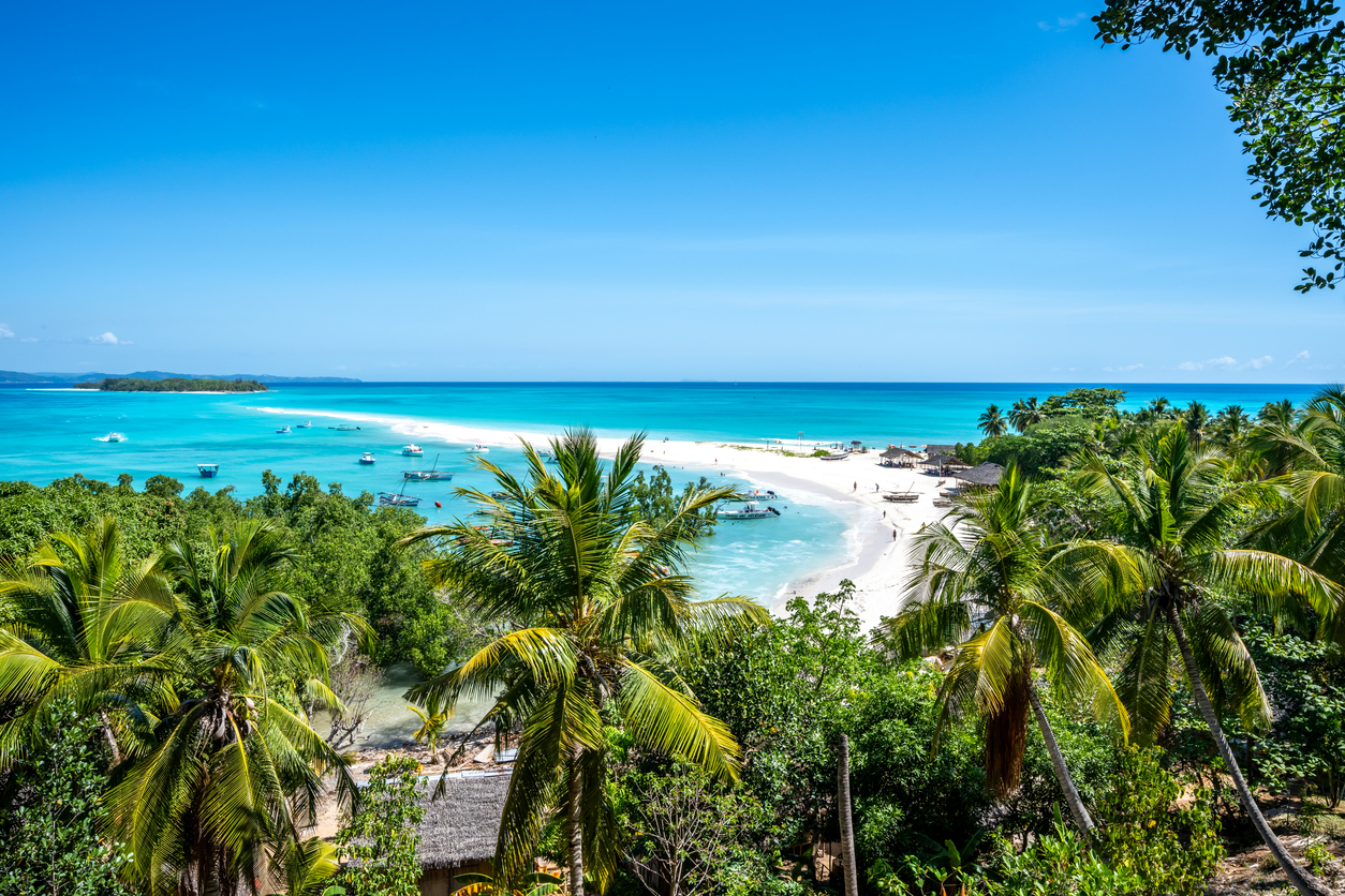 Von einem Aussichtspunkt sieht man einen langen weißen Strand, türkisfarbenes Wasser und kleine Boote.