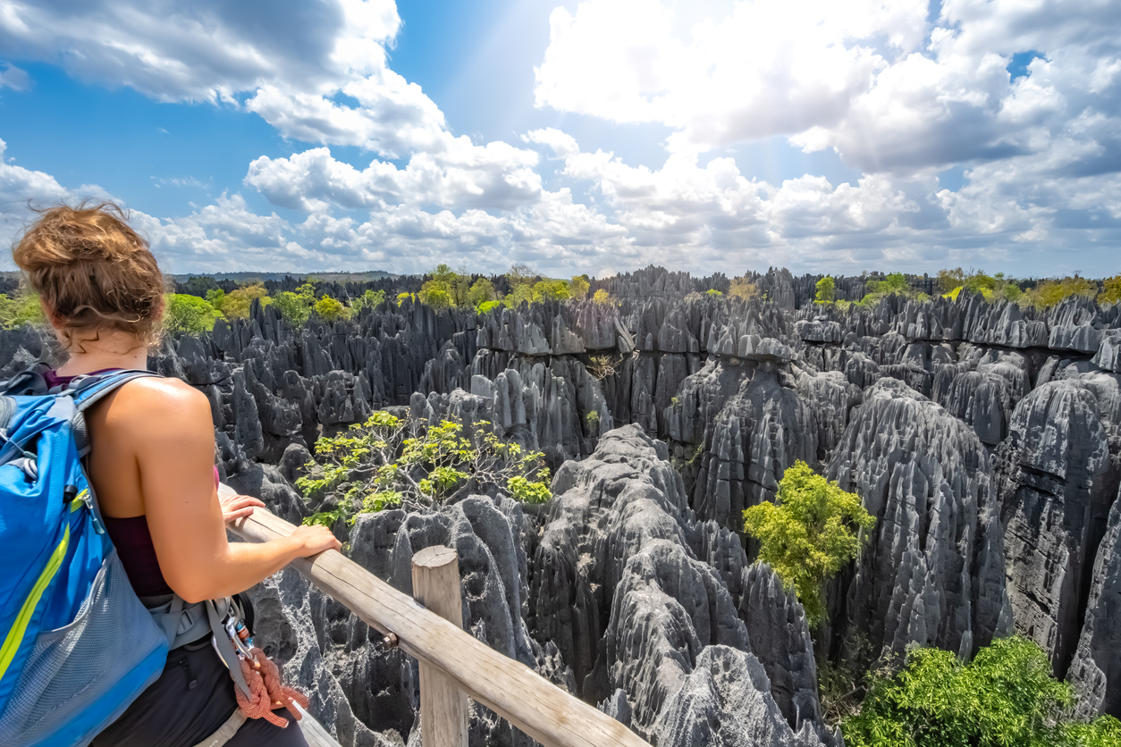 Eine Wanderin blickt von einer Plattform auf spitze Kalksteinfelsen auf Madagaskar.