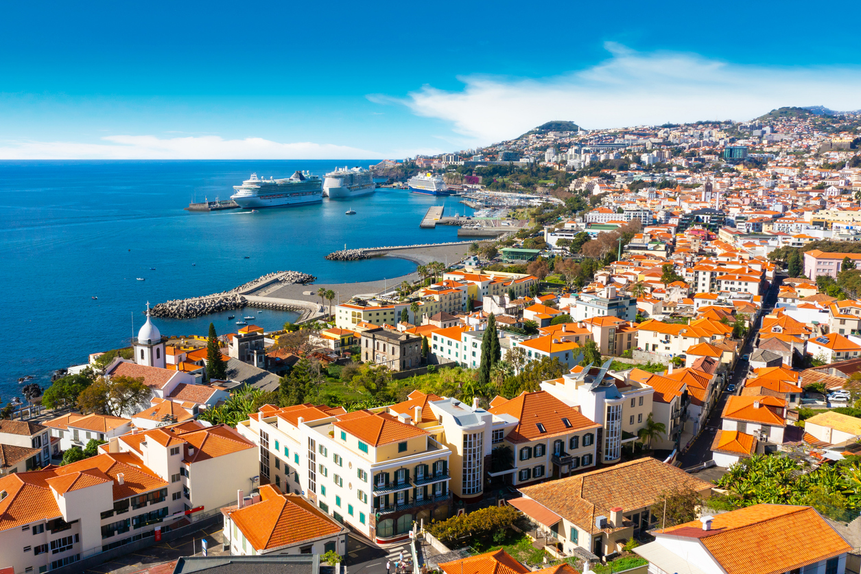 Funchal zeigt sich mit Hafen, Kreuzfahrtschiffen und roten Dächern an der Südküste Madeiras.