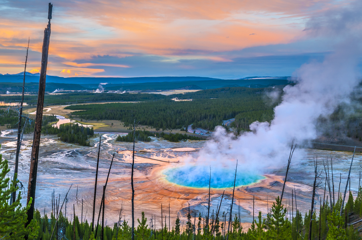 Ein dampfender, türkisblauer Thermalpool liegt in einer weiten Landschaft im Yellowstone Nationalpark.