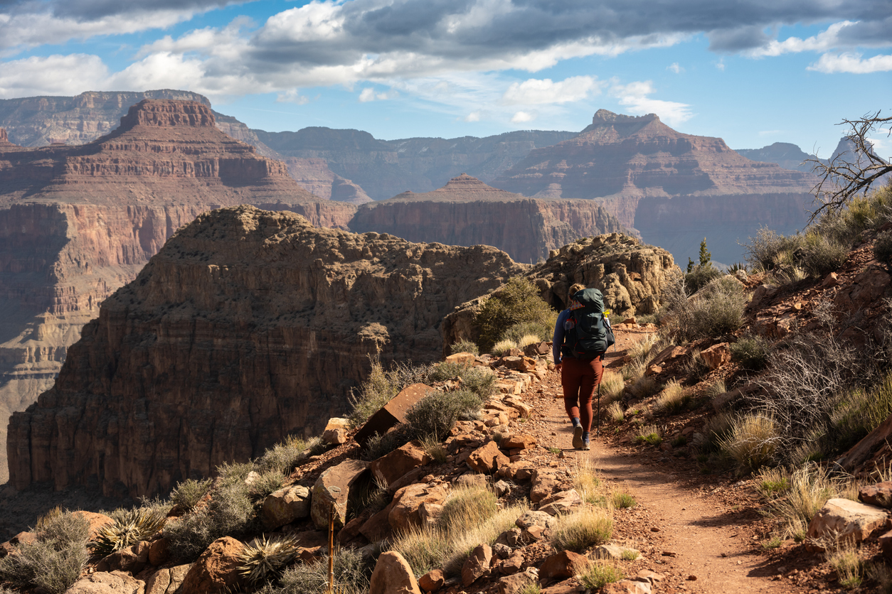 Eine Person mit Rucksack läuft auf einem schmalen Trail am Grand Canyon entlang.