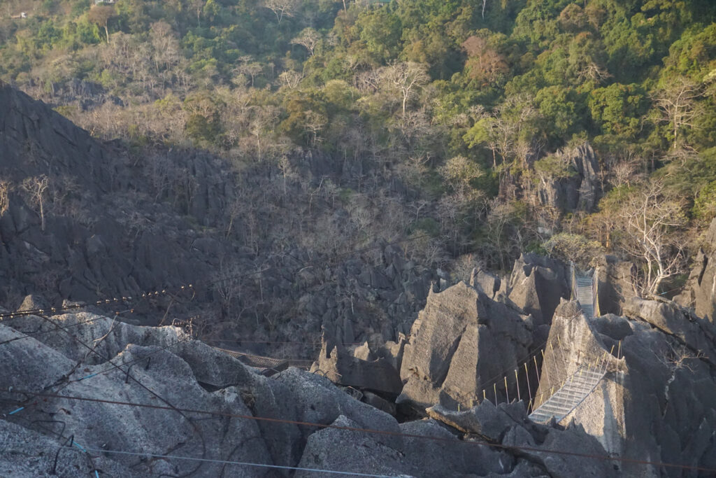 Ein schmaler Steg führt durch schroffe Felsen in eine bewaldete Schlucht.