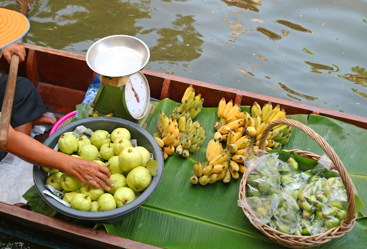Ein Markthändler verkauft Guaven und Bananen aus einem Holzboot am Khlong Lat Mayom Floating Market.
