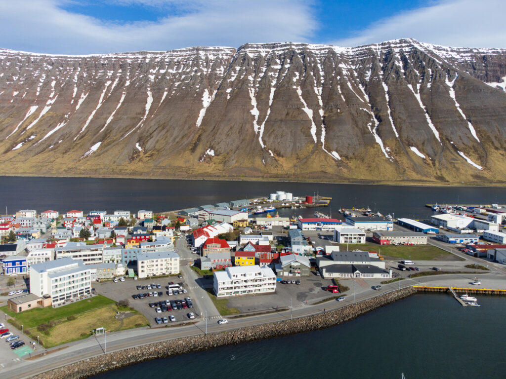 Luftaufnahme von Ísafjörður mit Hafen, bunten Häusern und steilen Bergen am Fjordufer.