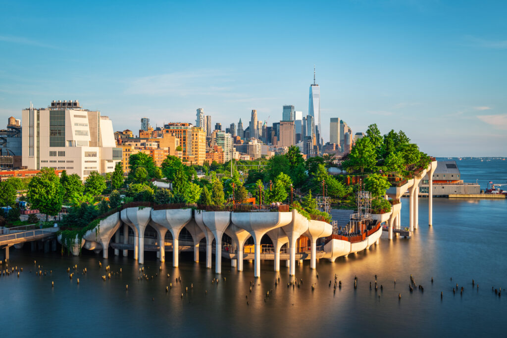 Ein bepflanzter Park auf Stelzen ragt ins Wasser, dahinter die Skyline von New York.