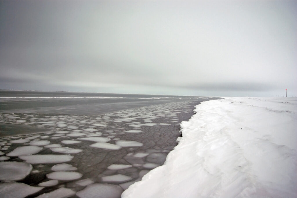 Treibeis liegt auf dunklem Wasser neben einer hohen Schneekante in Utqiaġvik (Barrow).
