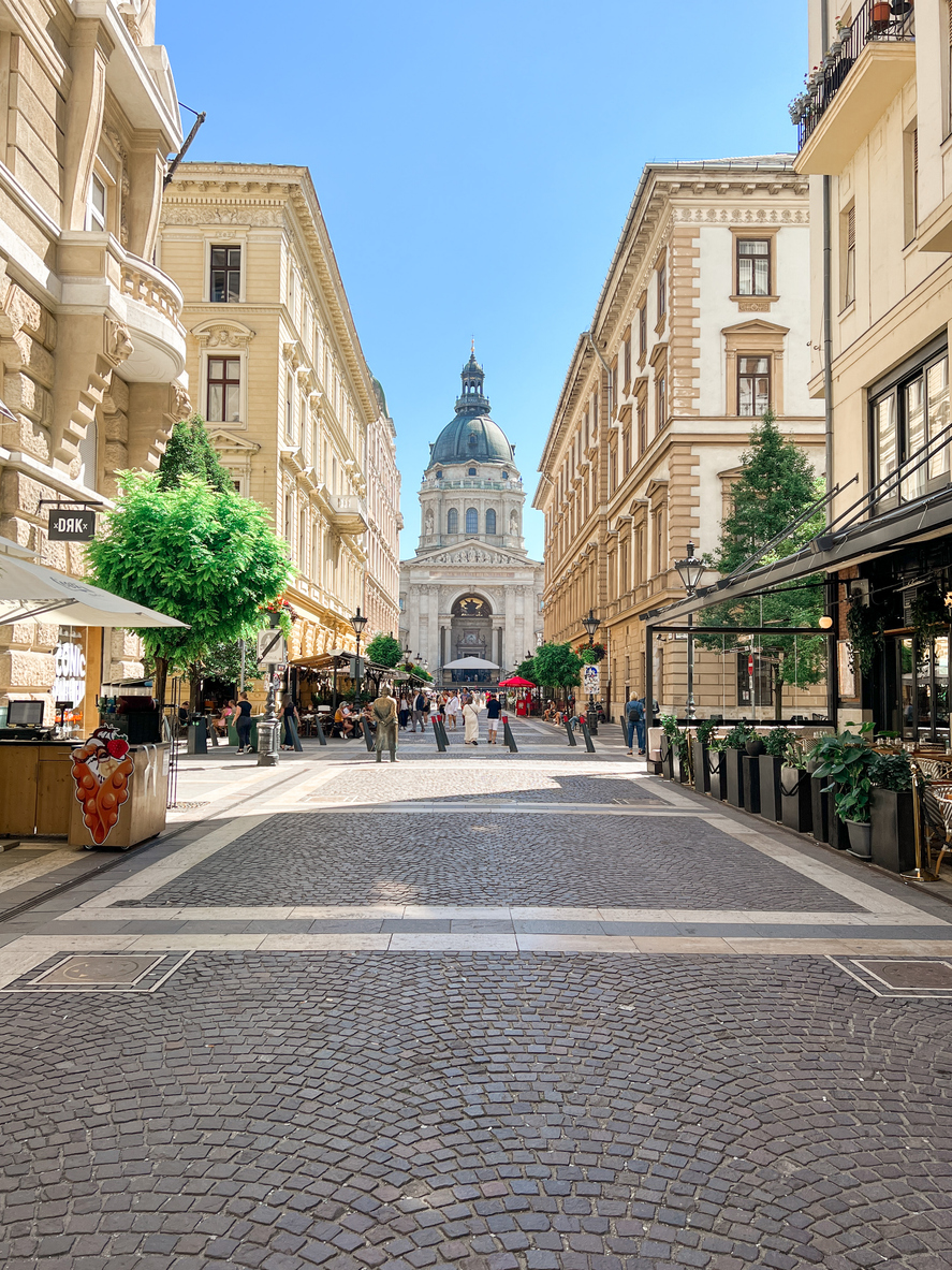 Eine breite Fußgängerzone mit Cafés führt auf eine große Kuppelkirche in Budapest zu.