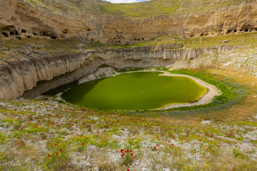 Ein runder Krater mit steilen Felswänden umschließt einen grün schimmernden See.