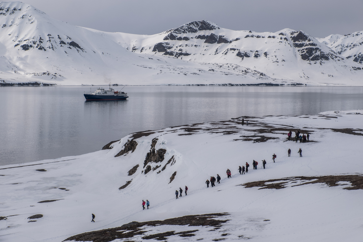 Menschen wandern über eine schneebedeckte Küste mit Blick auf ein Schiff in Nunavut.
