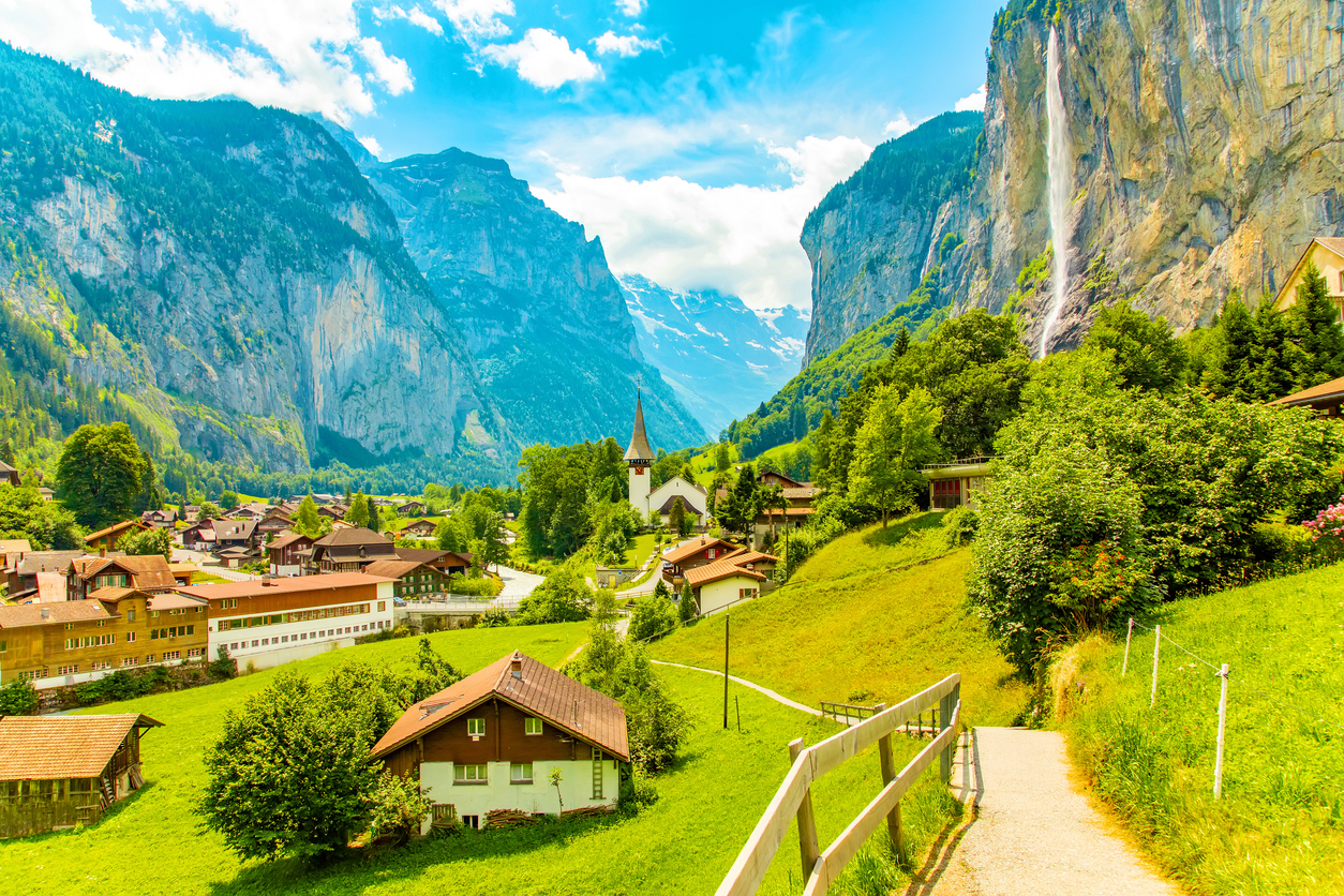 Blick über Lauterbrunnen mit Chalets, Wiesen, einer Kirche und einem hohen Wasserfall an einer Felswand.