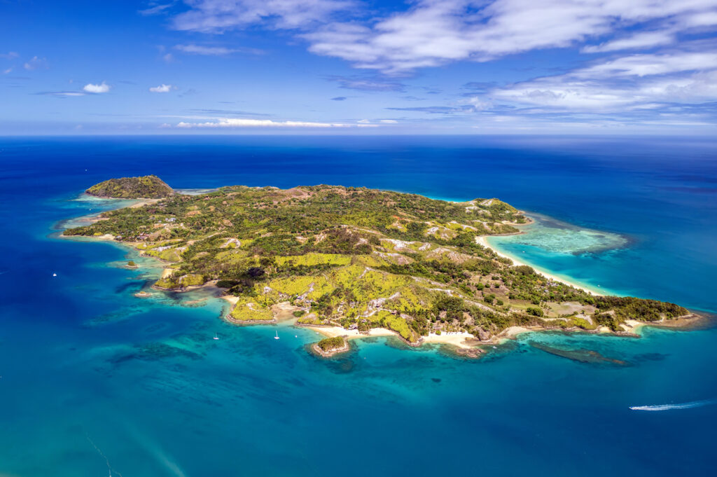 Aus der Luft sieht man eine grüne Insel mit hellen Stränden und Riffen im klaren Wasser.