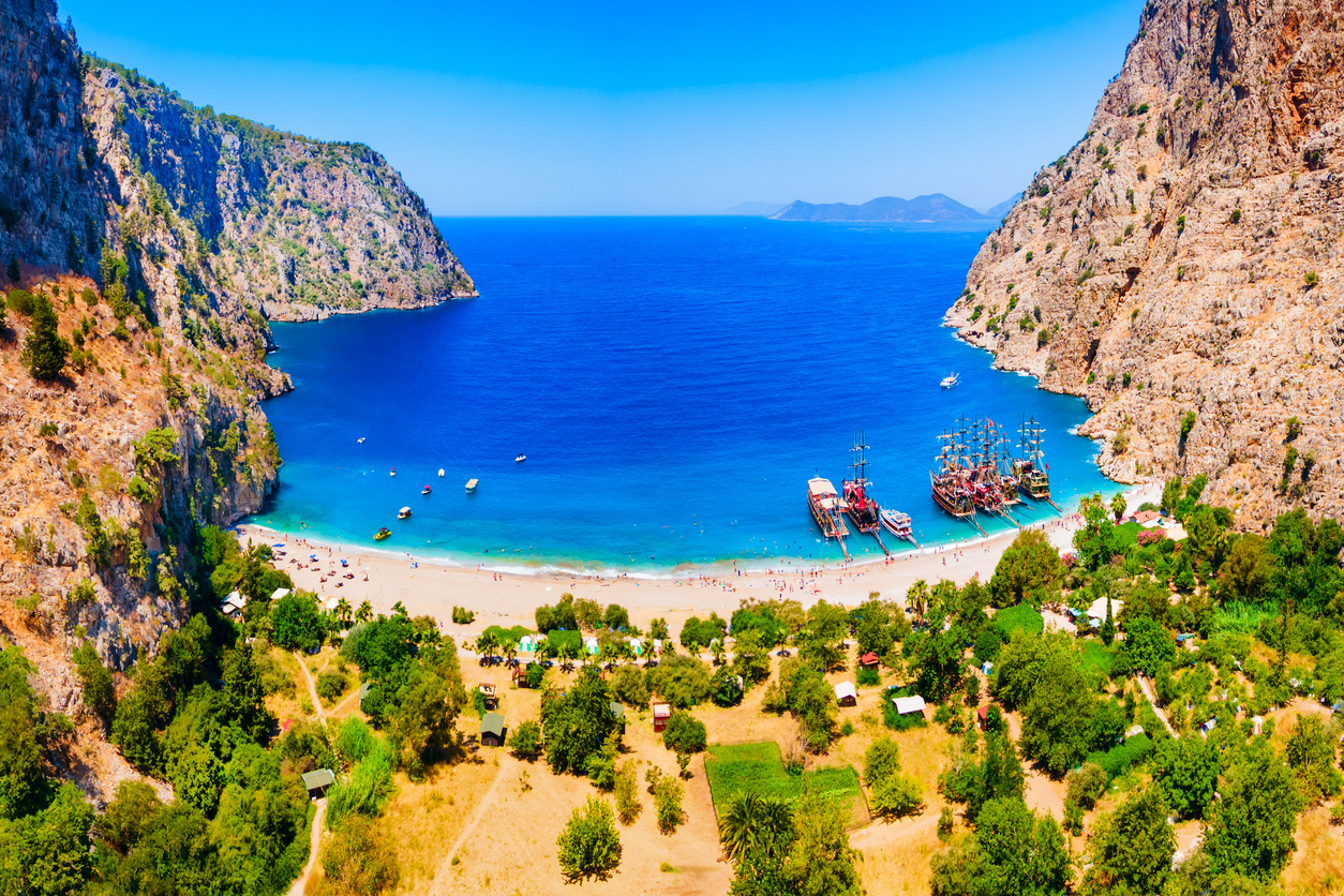 Eine helle Sandbucht liegt zwischen hohen Felsen und tiefblauem Meer.