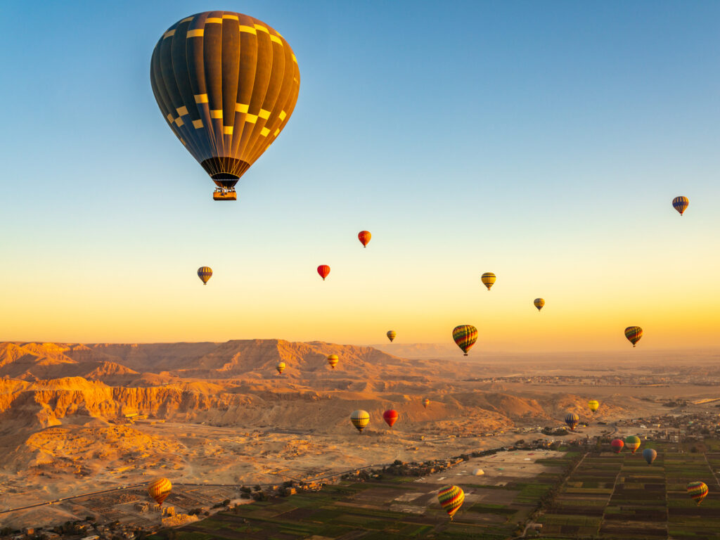 Viele bunte Heißluftballons schweben über der Wüstenlandschaft und den Feldern bei Luxor.