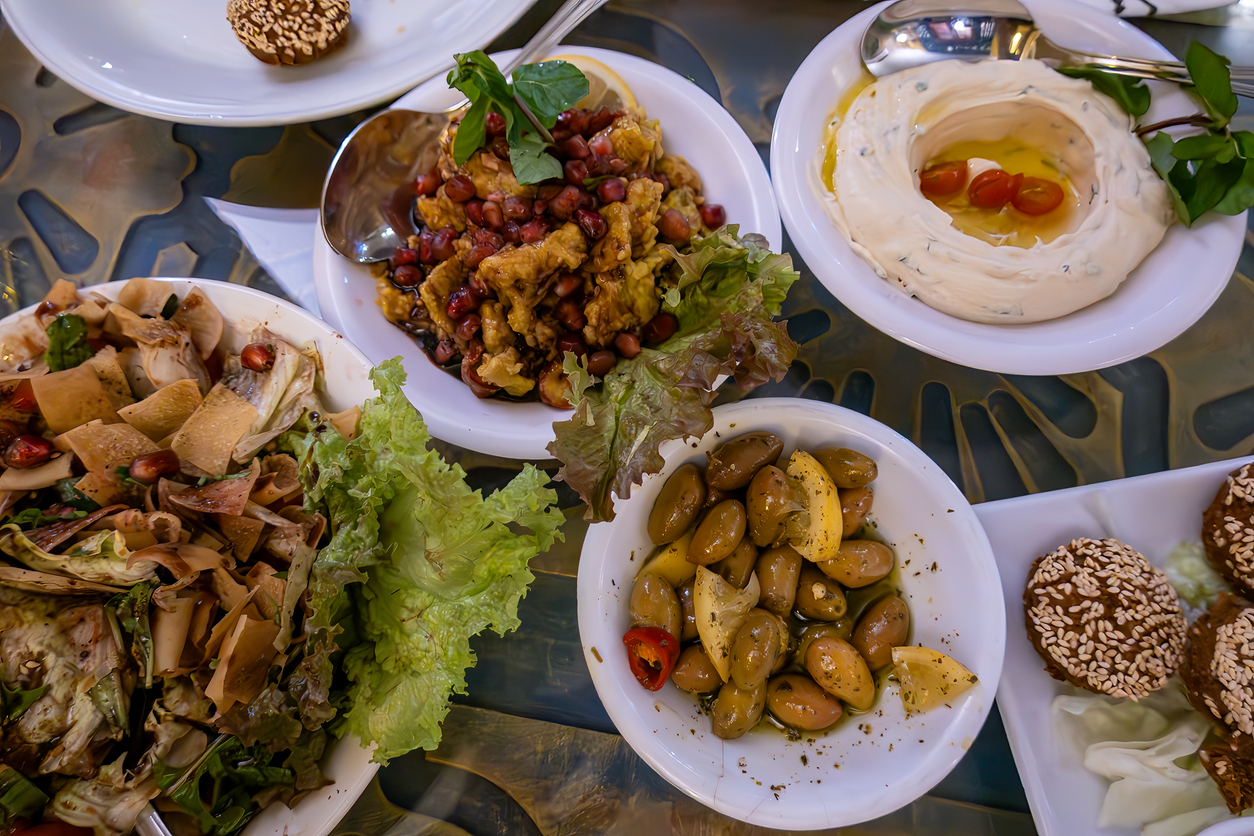 Auf einem Tisch stehen mehrere Teller mit Hummus, Oliven, Salat und kleinen Gebäckstücken.