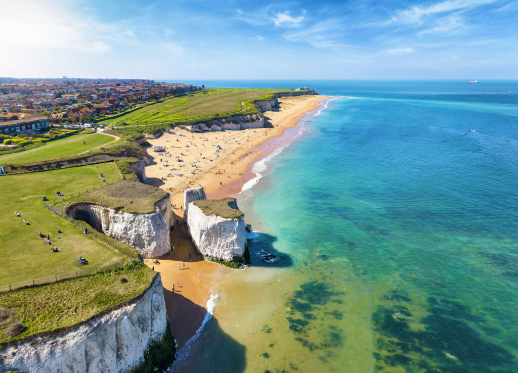Luftaufnahme von weißen Klippen, einem Sandstrand und türkisblauem Meer.