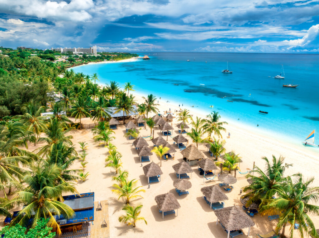 Ein tropischer Strand mit Palmen und Strohdachhütten liegt an einer türkisblauen Lagune auf Sansibar.