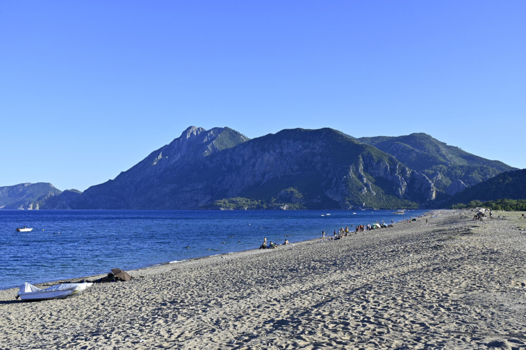 Ein breiter Sandstrand liegt am Meer, dahinter ragen dunkle Berge in den Himmel.