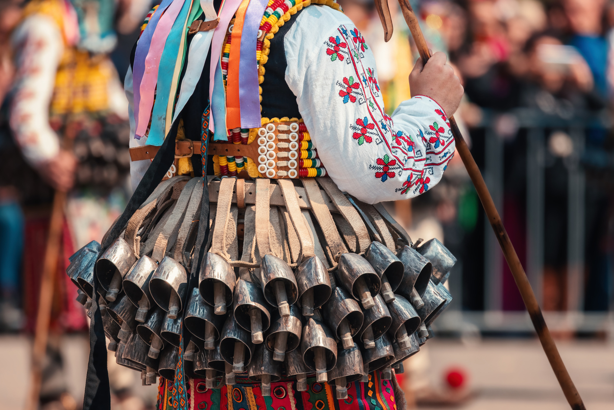 Eine Person trägt eine bestickte Tracht mit vielen Metallglocken und bunten Bändern als bulgarische Folklore.