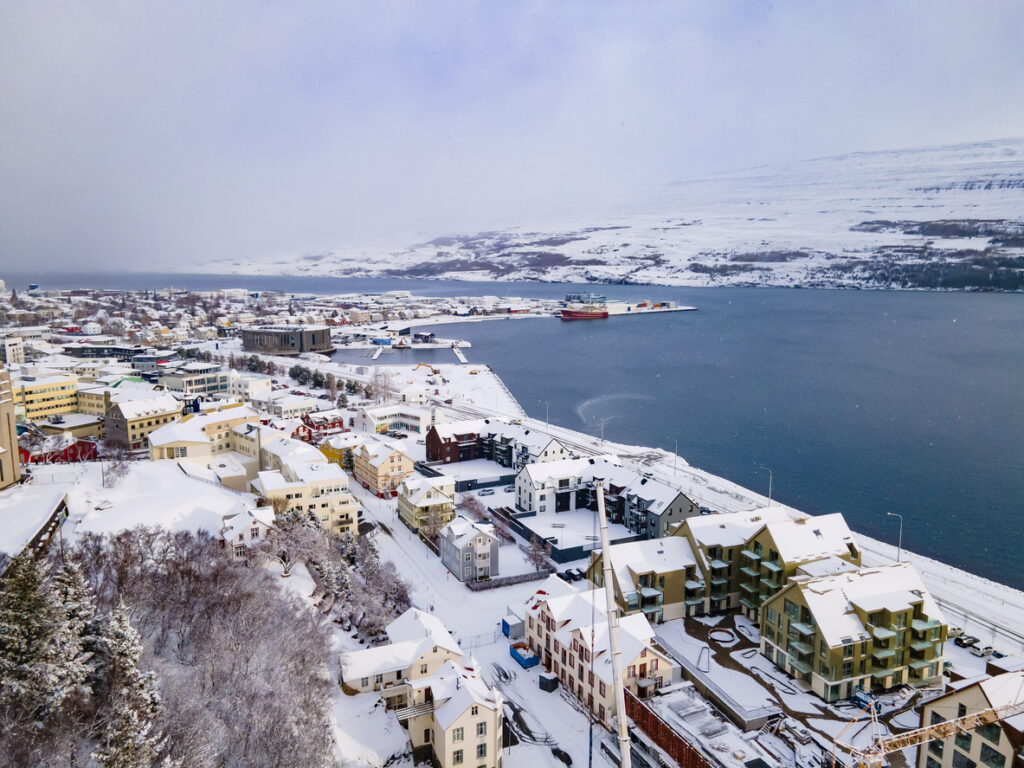 Verschneite Häuser von Akureyri liegen am Fjord unter einem grauen Winterhimmel.