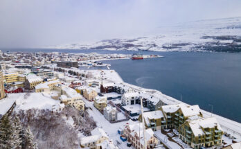 Verschneite Häuser von Akureyri liegen am Fjord unter einem grauen Winterhimmel.
