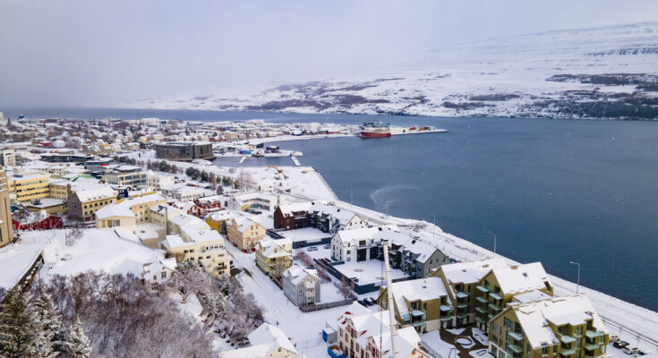 Verschneite Häuser von Akureyri liegen am Fjord unter einem grauen Winterhimmel.