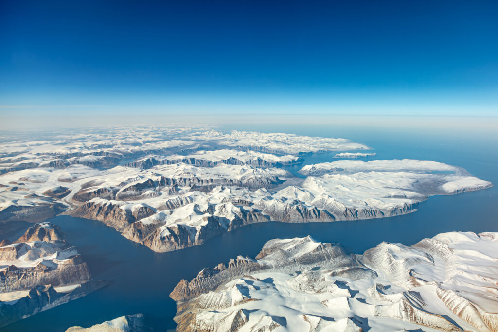 Eine Luftaufnahme zeigt schneebedeckte Berge und dunkles Wasser in Nunavut.