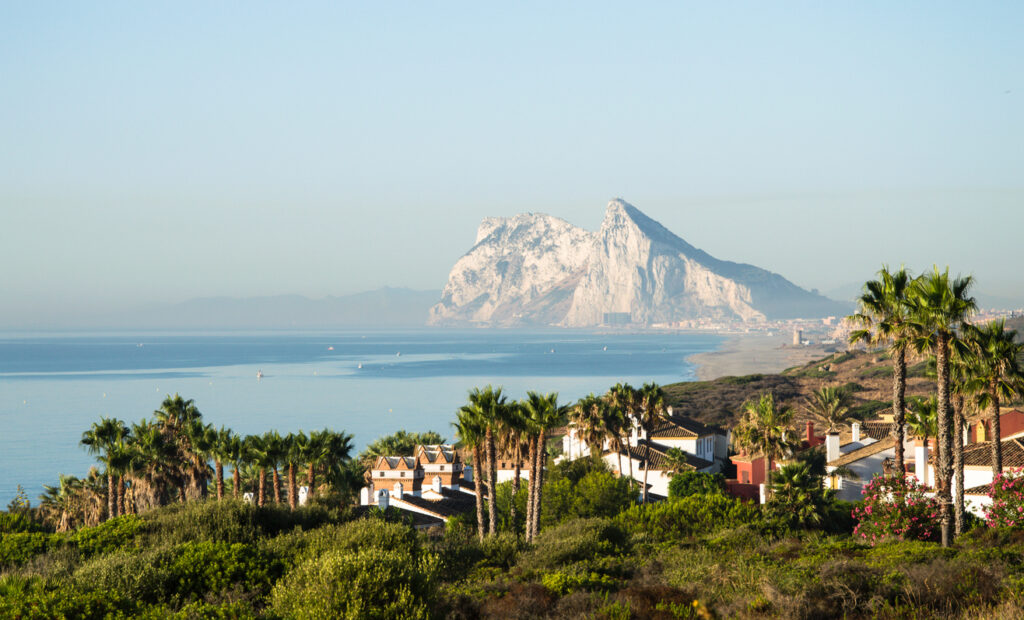 Palmen rahmen den Blick auf Gibraltar, während der Felsen in der Ferne aufragt.